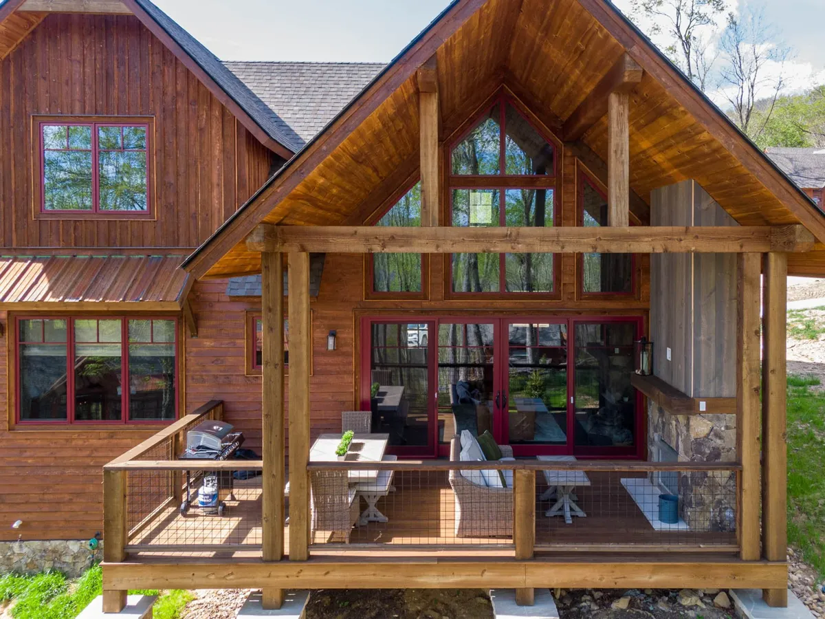 A cozy wooden deck extends from the home, featuring comfortable outdoor seating and large windows that visually connect the interior living space to the mountain surroundings. The deck offers open views of nature, inviting guests to relax with a morning coffee or a glass of wine at sunset.