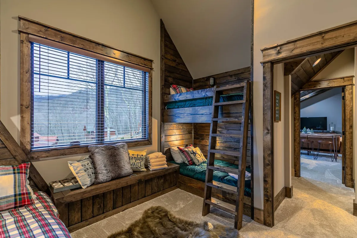 A cozy bunk room with multiple bunk beds, a large window offering mountain views, and a plush seating area. The decor is inviting and playful, making it an ideal retreat for families or groups of friends seeking comfort and togetherness.
