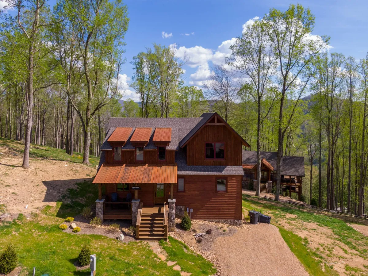The hero image shows a brand-new wooden house nestled among lush green trees, with inviting outdoor stairs leading up to a welcoming porch. The peaceful setting highlights the home's connection to nature and offers glimpses of scenic views perfect for sunsets, stargazing, and wildlife watching.