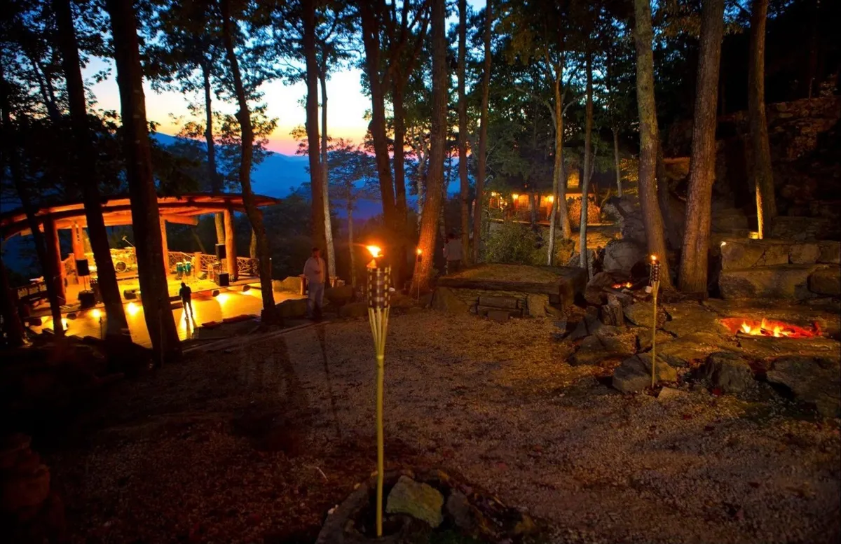 This inviting outdoor scene captures a fire pit surrounded by comfortable seating, with torches lighting the cozy gathering space next to a wooden structure. The natural setting is ideal for evening storytelling, unwinding after a day outdoors, and connecting with friends or family under the stars.