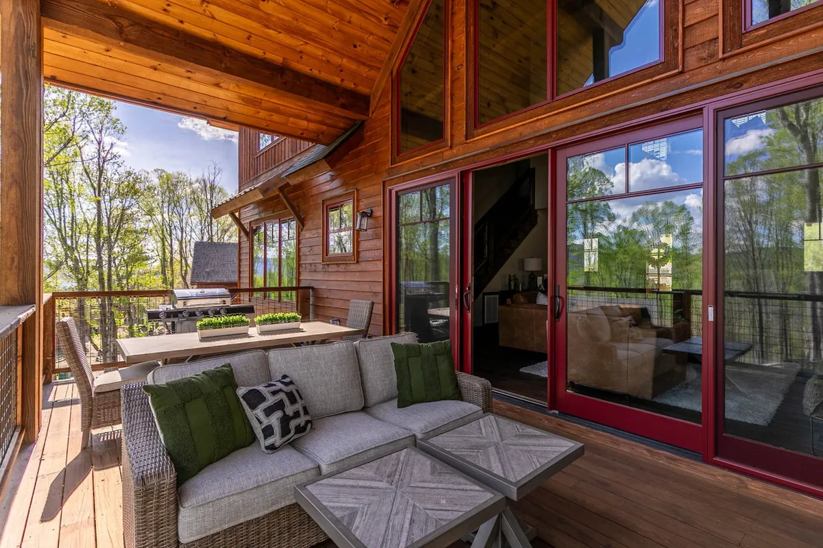 A welcoming wooden deck with outdoor seating, a dining table, and large glass doors connecting indoor and outdoor spaces. The setting is perfect for social gatherings, barbecues, and sunset watching, surrounded by natural beauty.