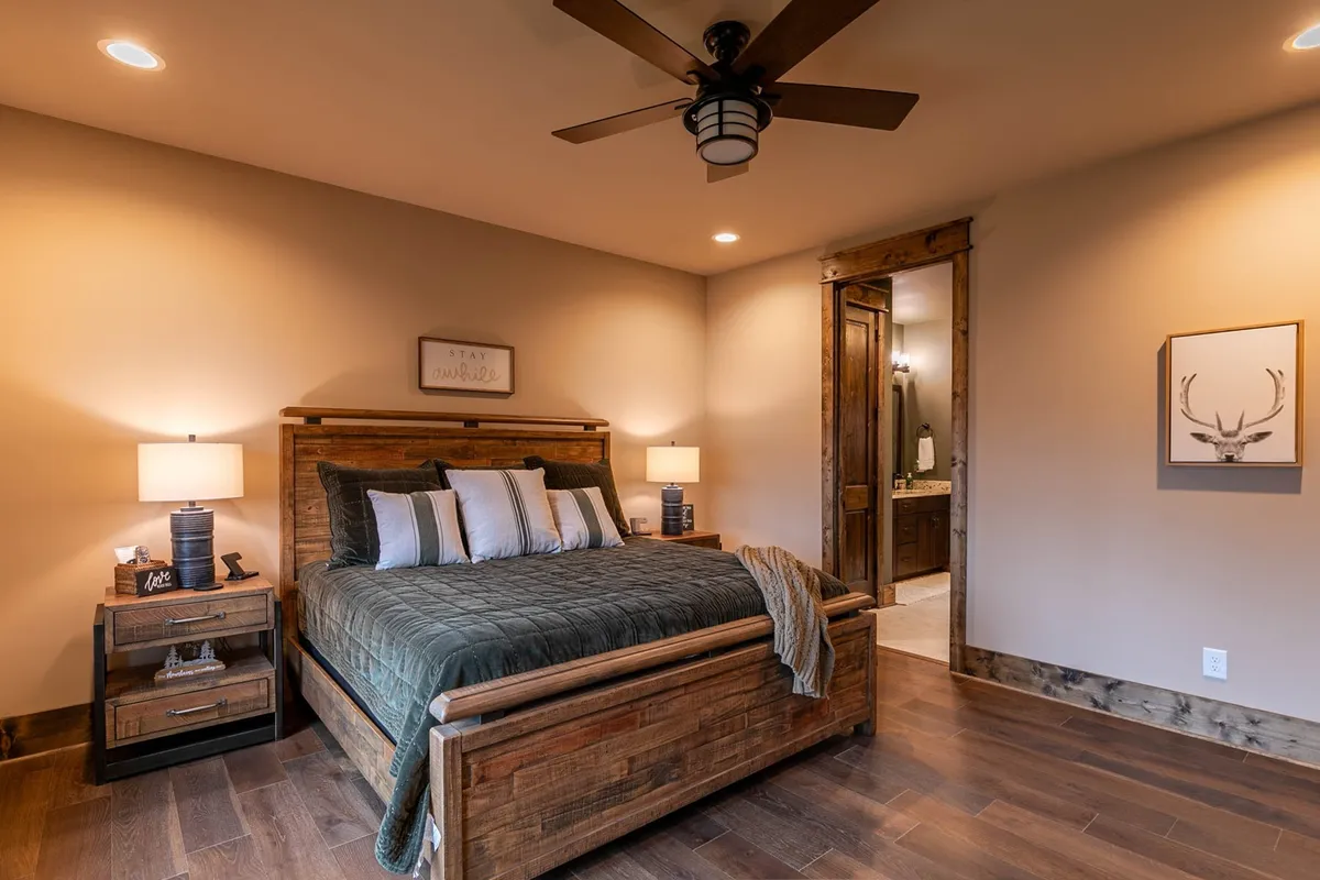 A warmly lit bedroom featuring a comfortable bed with crisp linens, matching nightstands, and tasteful wall decor. The doorway provides a glimpse into the rest of the home, and the room feels both spacious and private, ideal for relaxation after a day of adventure.