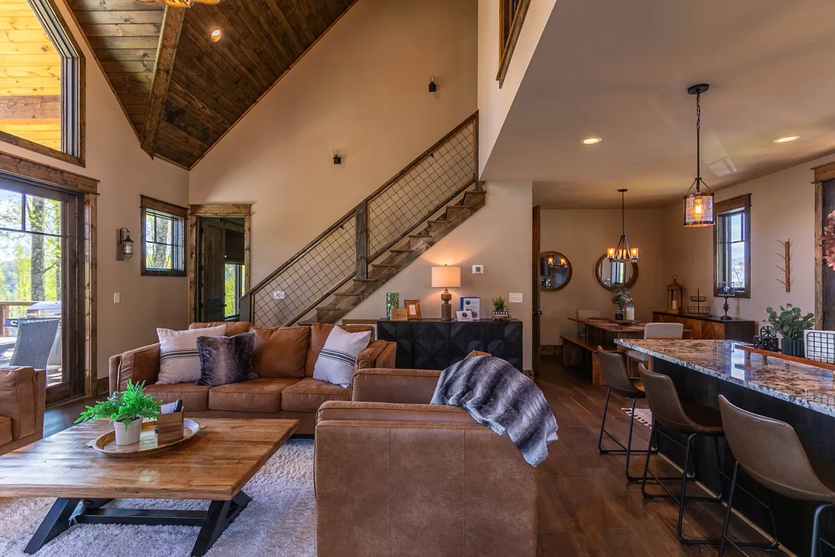 A warm, open-plan space featuring a plush sofa, a welcoming dining table, a stylish staircase, and a bar counter. The layout invites family and friends to gather for meals, relaxation by the fire, or entertaining guests.