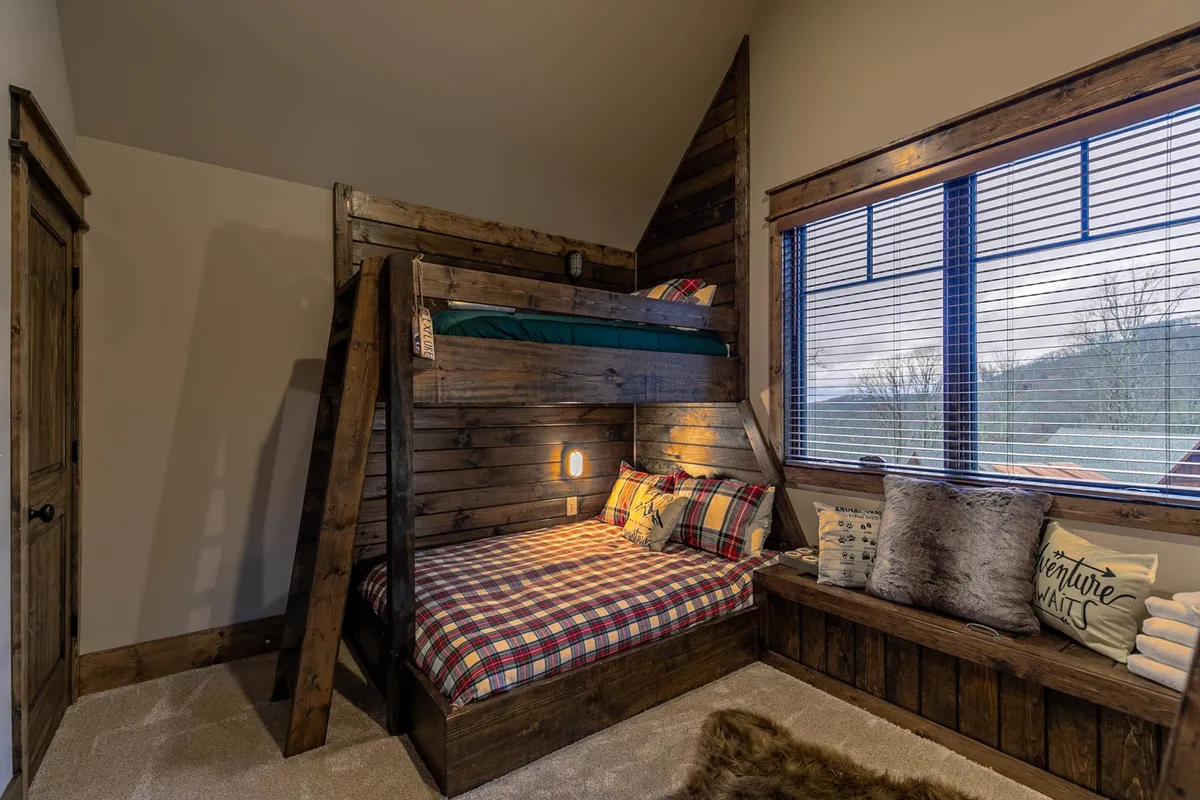 This cozy interior shows a bunk bed with plaid bedding and a window view. The space hints at a playful, family-friendly environment where games and bonding can happen, especially on rainy days or during relaxed evenings.