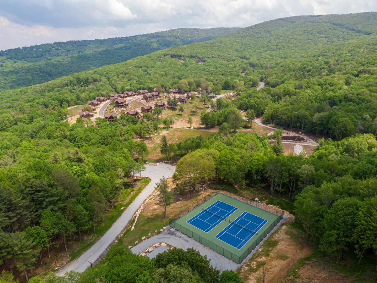 This image features well-maintained tennis courts surrounded by rolling greenery and majestic mountain views in the backdrop. A scenic road winds nearby, suggesting access to outdoor activities and community amenities within the Eagles Nest development.