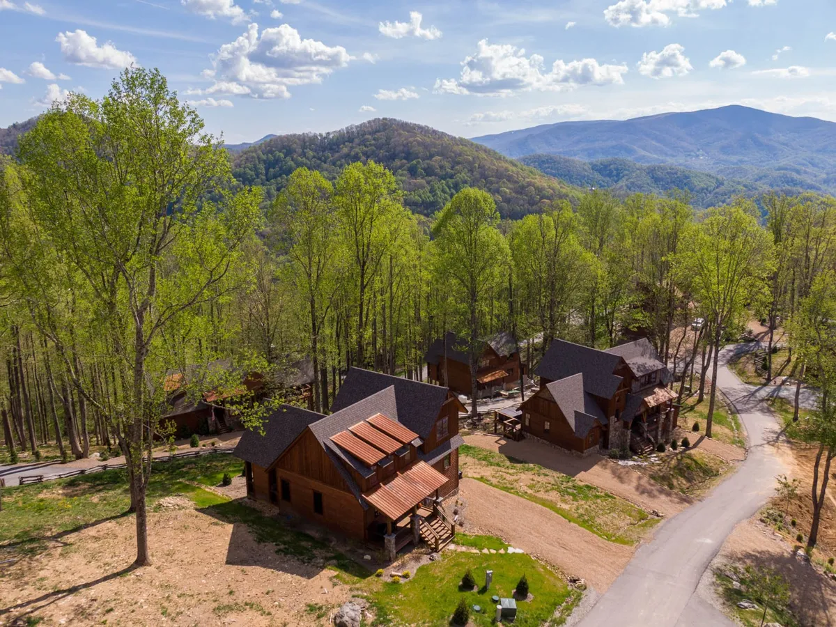 This image showcases a cluster of rustic wooden cabins nestled among lush green trees, with a spectacular mountain backdrop. The setting evokes a sense of outdoor adventure and the serene beauty of the high country, perfect for hiking, nature walks, or simply enjoying the views after a day of mountain activities.