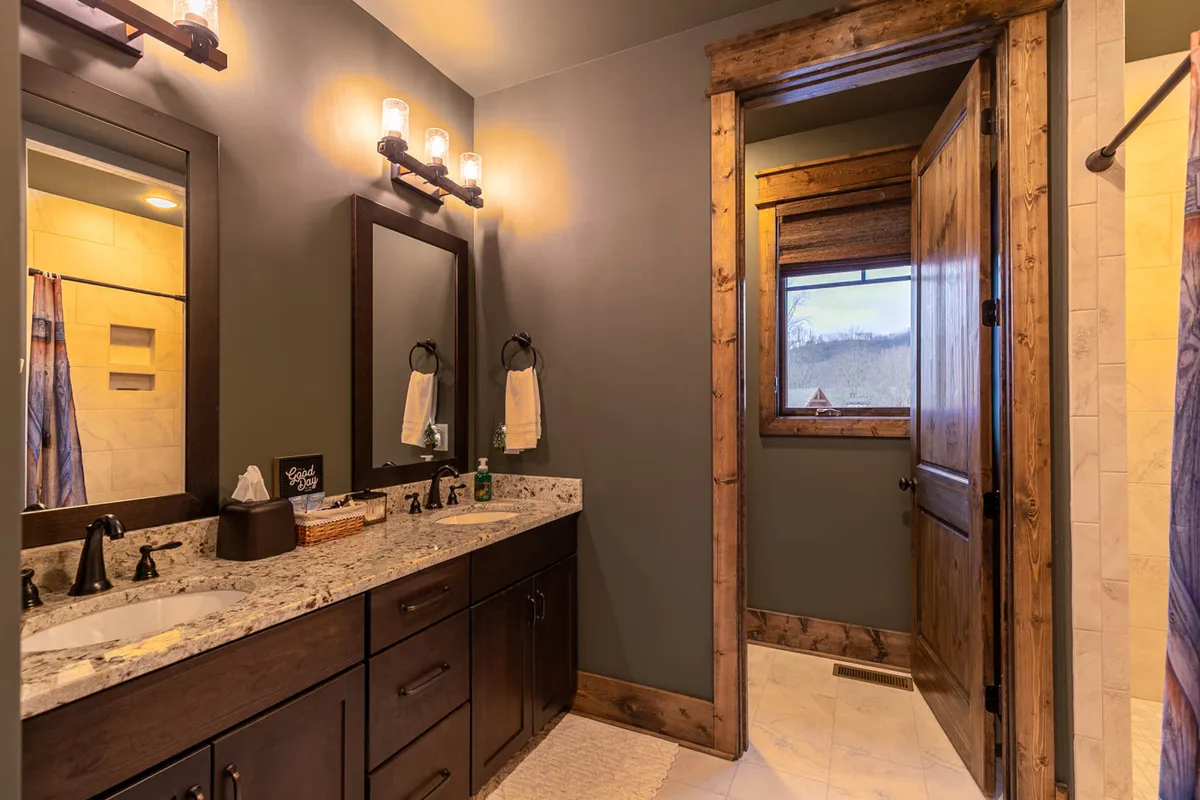 A serene bathroom scene with double granite vanities, stylish lighting, and large mirrors. A window softly illuminates the space, creating a spa-like environment ideal for unwinding and personal care.
